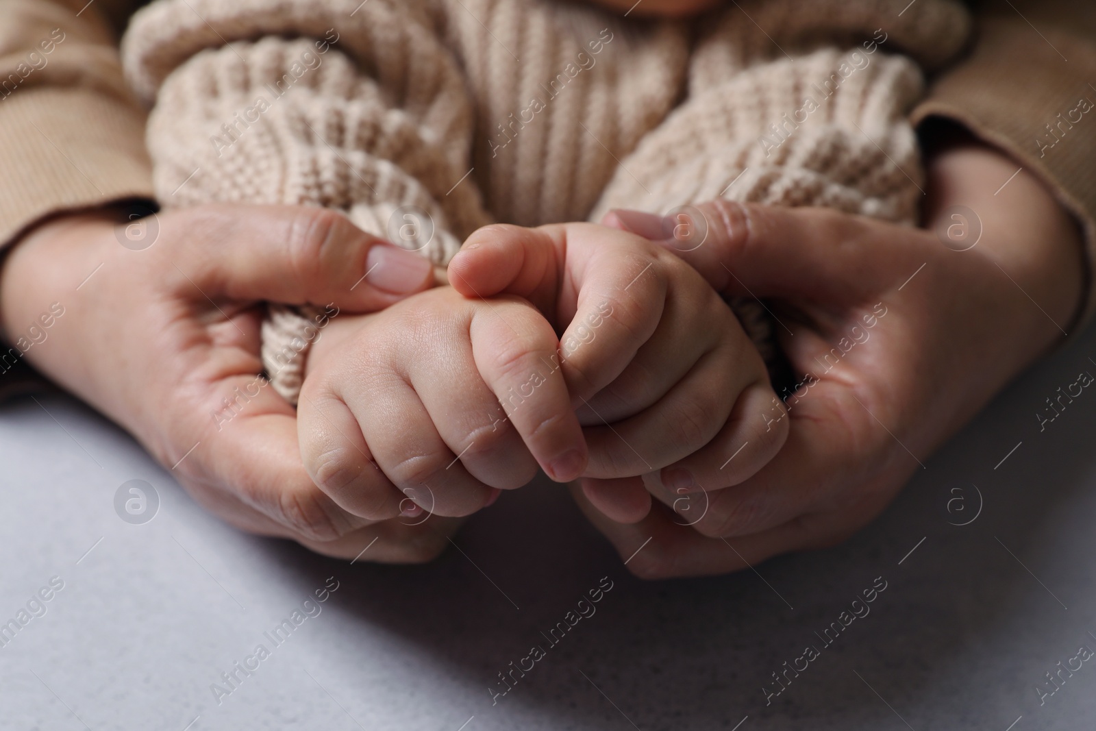 Photo of Woman holding hands with her little daughter at light grey table, closeup