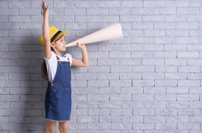Photo of Adorable little girl with paper megaphone on brick wall background