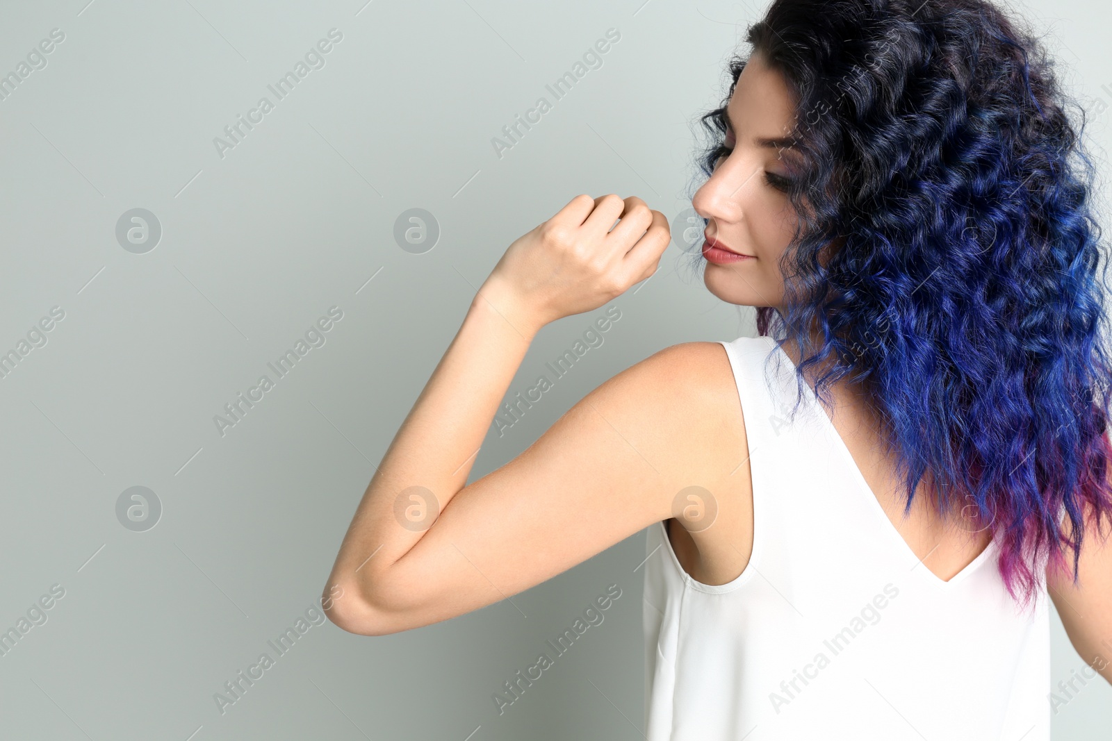 Photo of Young woman with bright dyed hair on grey background, back view. Space for text