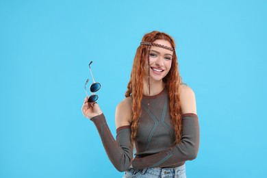 Photo of Stylish young hippie woman with sunglasses on light blue background