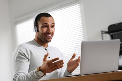 Young man with headphones having video chat via laptop at table in office