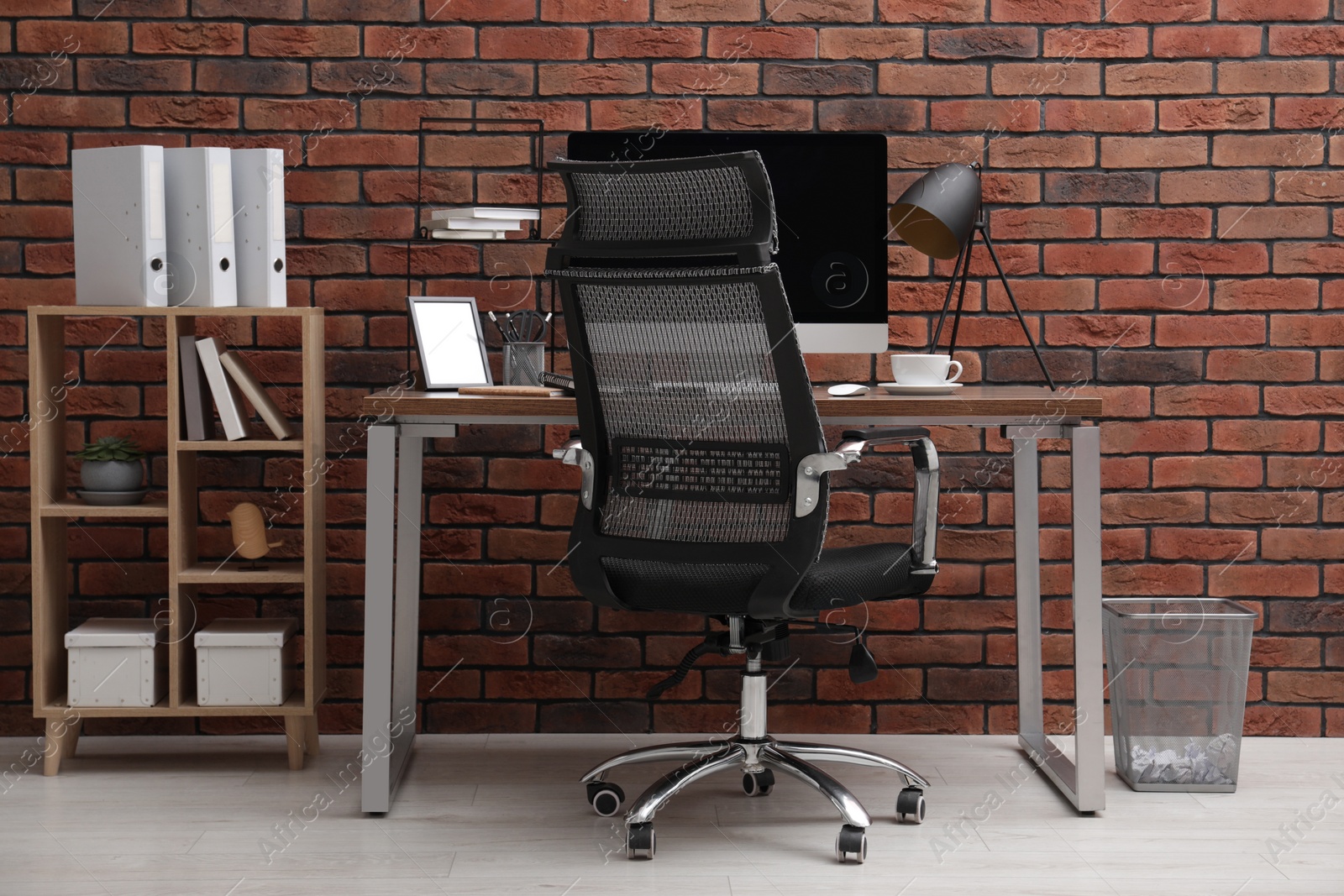 Photo of Cosy workspace with computer on desk, chair and bookcase near brick wall at home