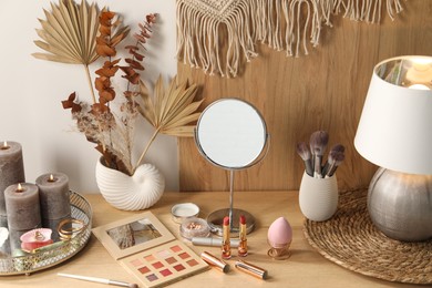 Makeup products, mirror and decor on wooden dressing table