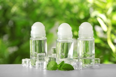 Photo of Deodorant containers, ice cubes and mint on white wooden table against blurred background