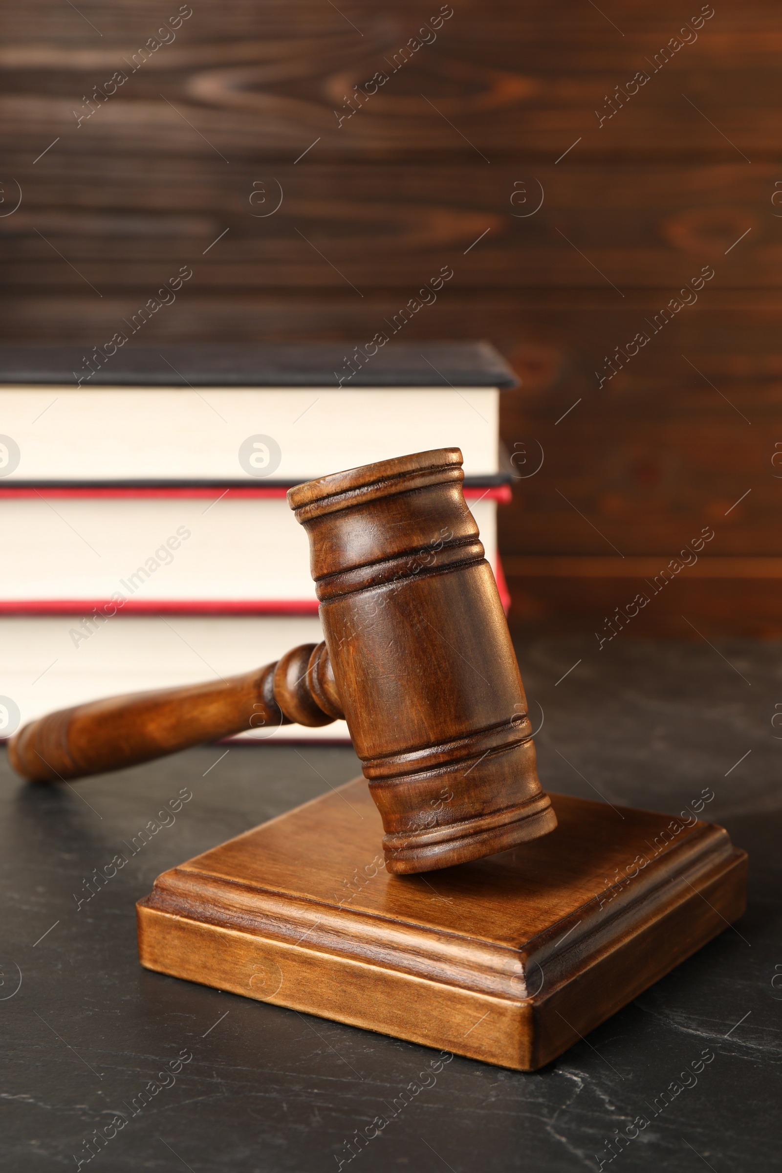 Photo of Wooden gavel and stack of books on dark textured table, closeup