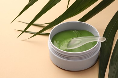 Photo of Jar of under eye patches with spoon and palm leaves on beige background, space for text. Cosmetic product