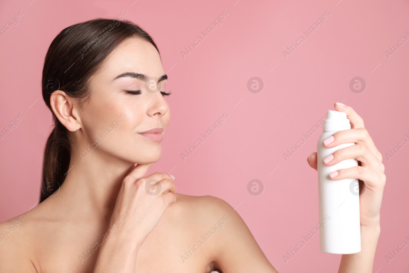 Photo of Young woman with bottle of thermal water on color background. Cosmetic product