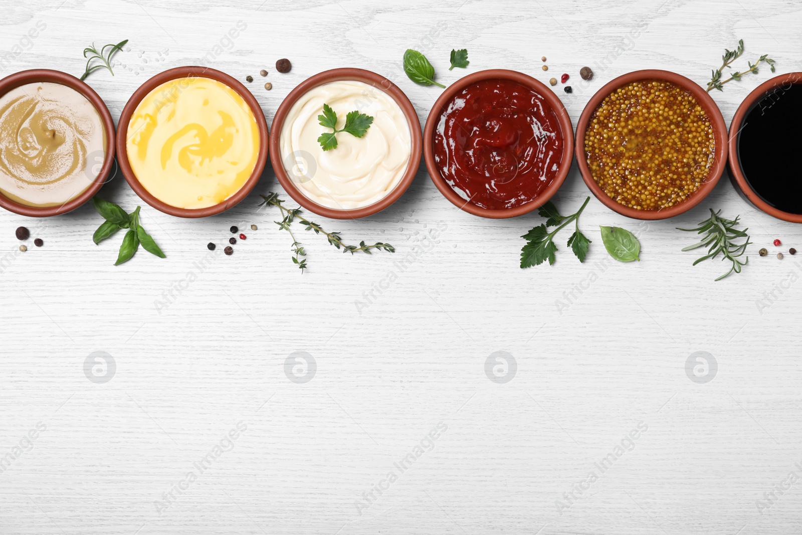 Photo of Many different sauces and herbs on white wooden table, flat lay. Space for text