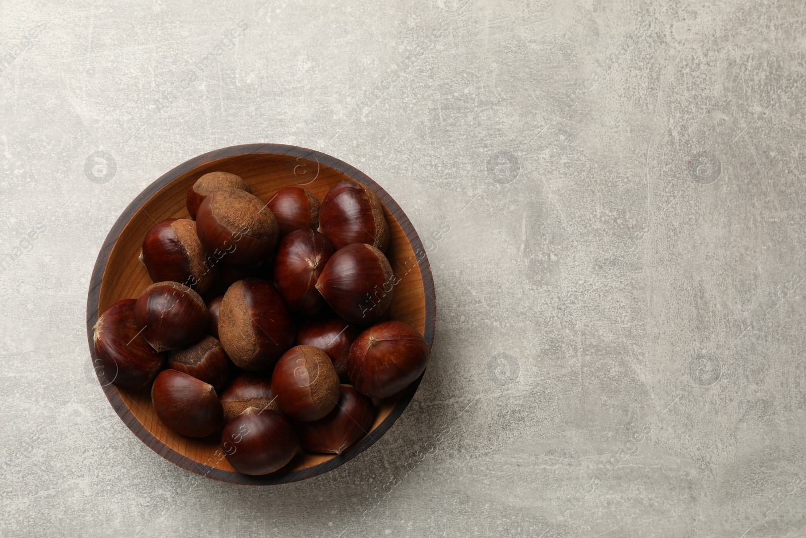 Photo of Roasted edible sweet chestnuts in bowl on light grey table, top view. Space for text