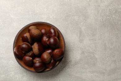 Photo of Roasted edible sweet chestnuts in bowl on light grey table, top view. Space for text