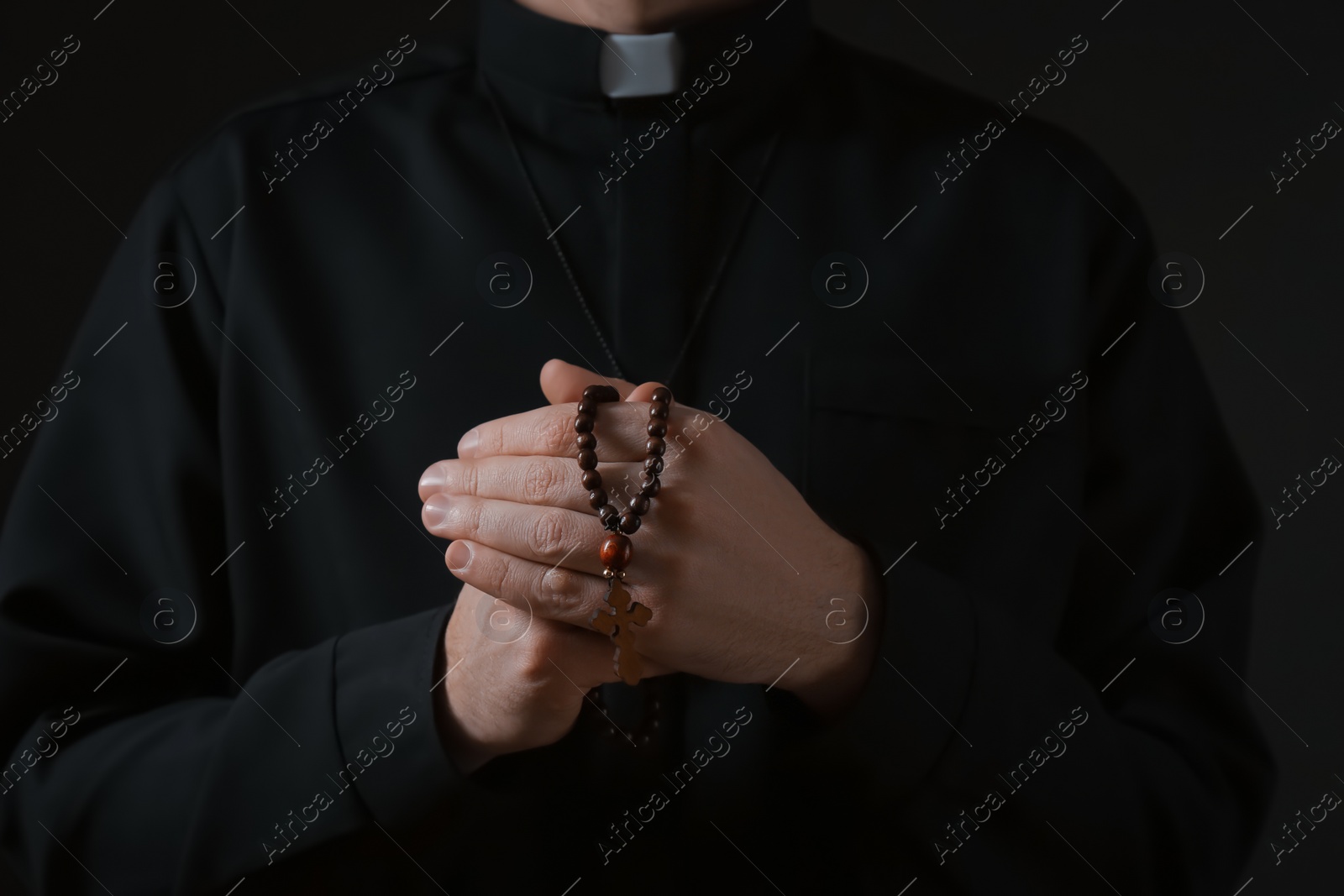 Photo of Priest with beads praying on dark background, closeup