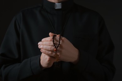 Photo of Priest with beads praying on dark background, closeup