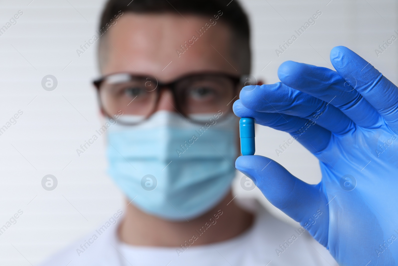 Photo of Doctor holding pill on light background, selective focus. Space for text