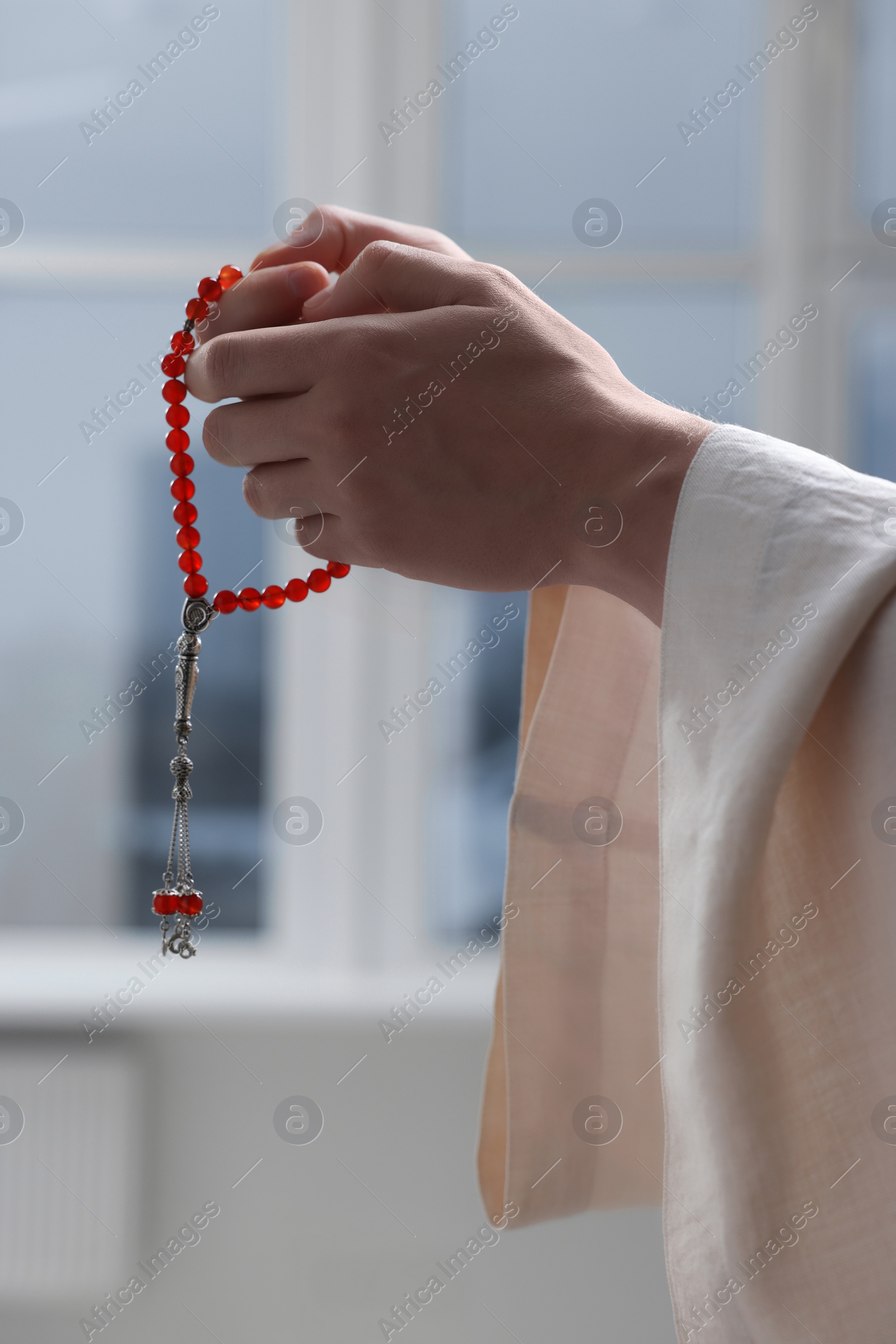 Photo of Muslim man with misbaha praying near window indoors, closeup