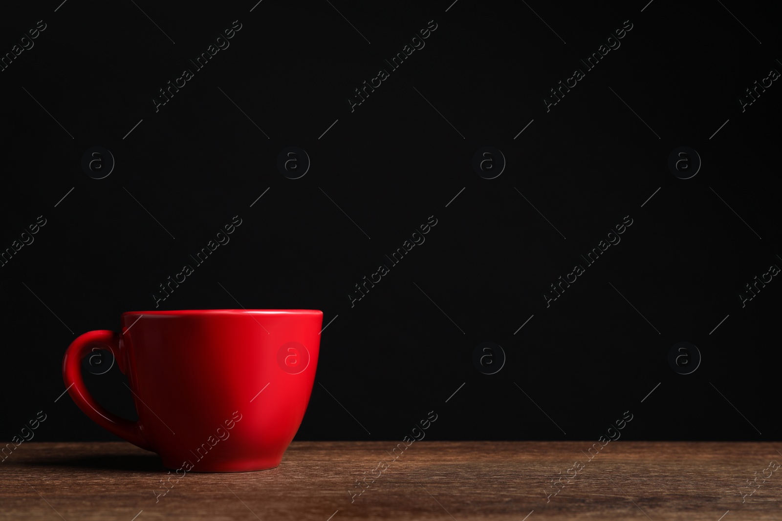 Photo of Red cup on wooden table against black background, space for text