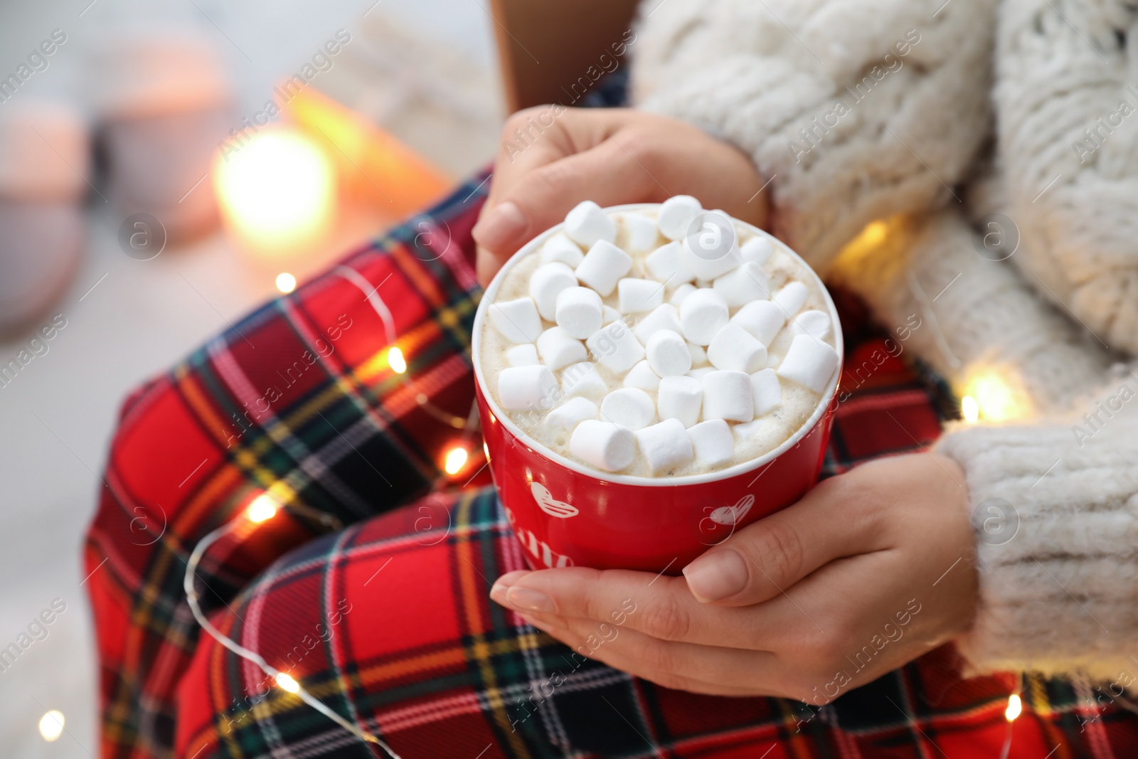 Photo of Woman holding cup of hot drink with marshmallows indoors, closeup. Magic Christmas atmosphere