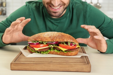 Photo of Hungry man and tasty sandwich on table, closeup
