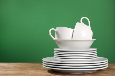 Set of clean dishware on wooden table against green background, space for text