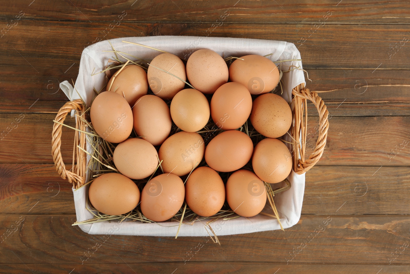 Photo of Raw chicken eggs in wicker basket on wooden table, top view