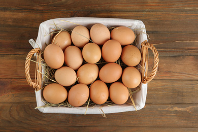 Raw chicken eggs in wicker basket on wooden table, top view