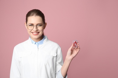Female dentist holding tooth model on color background. Space for text