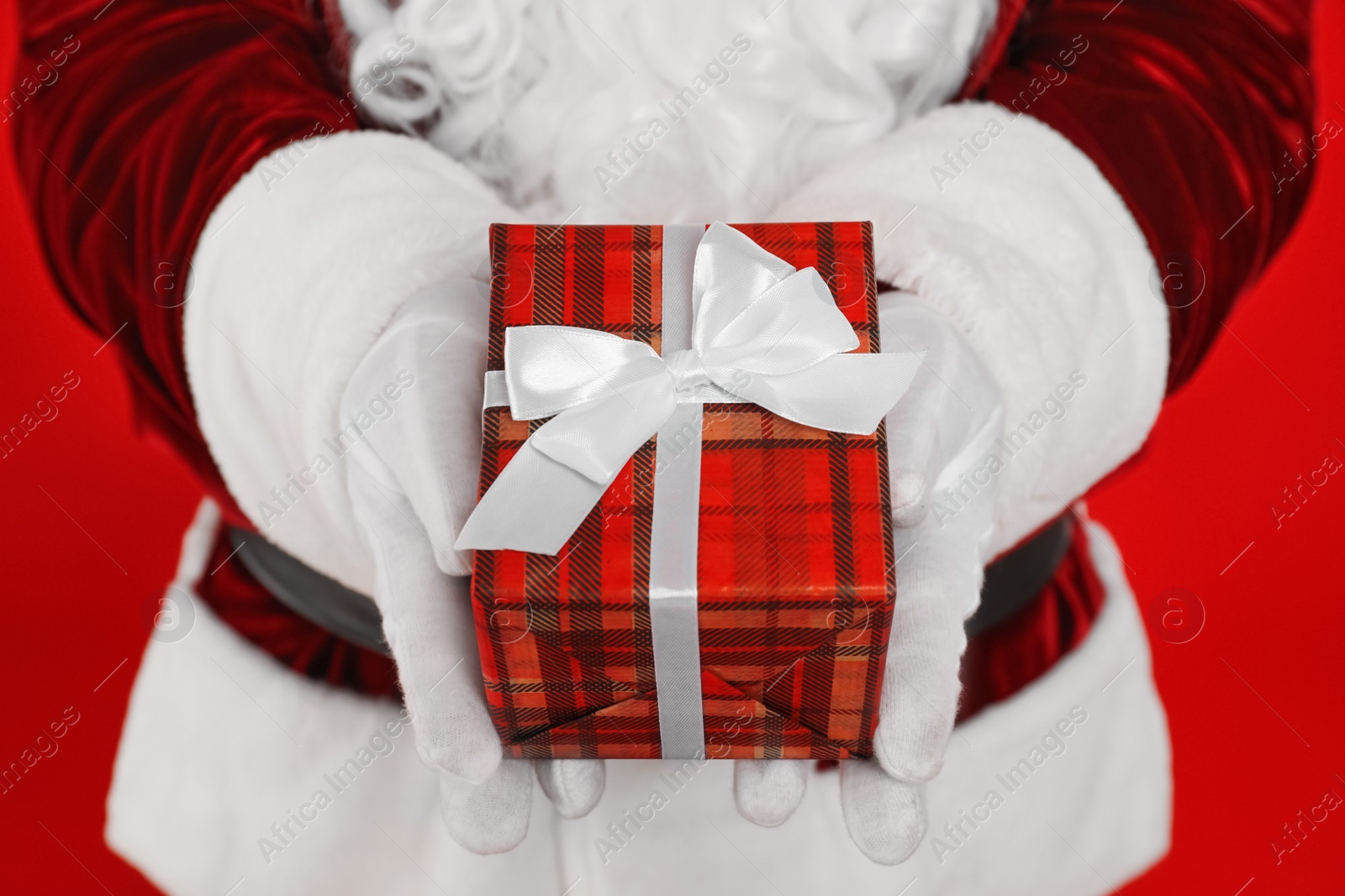 Photo of Santa Claus holding Christmas gift on red background, closeup