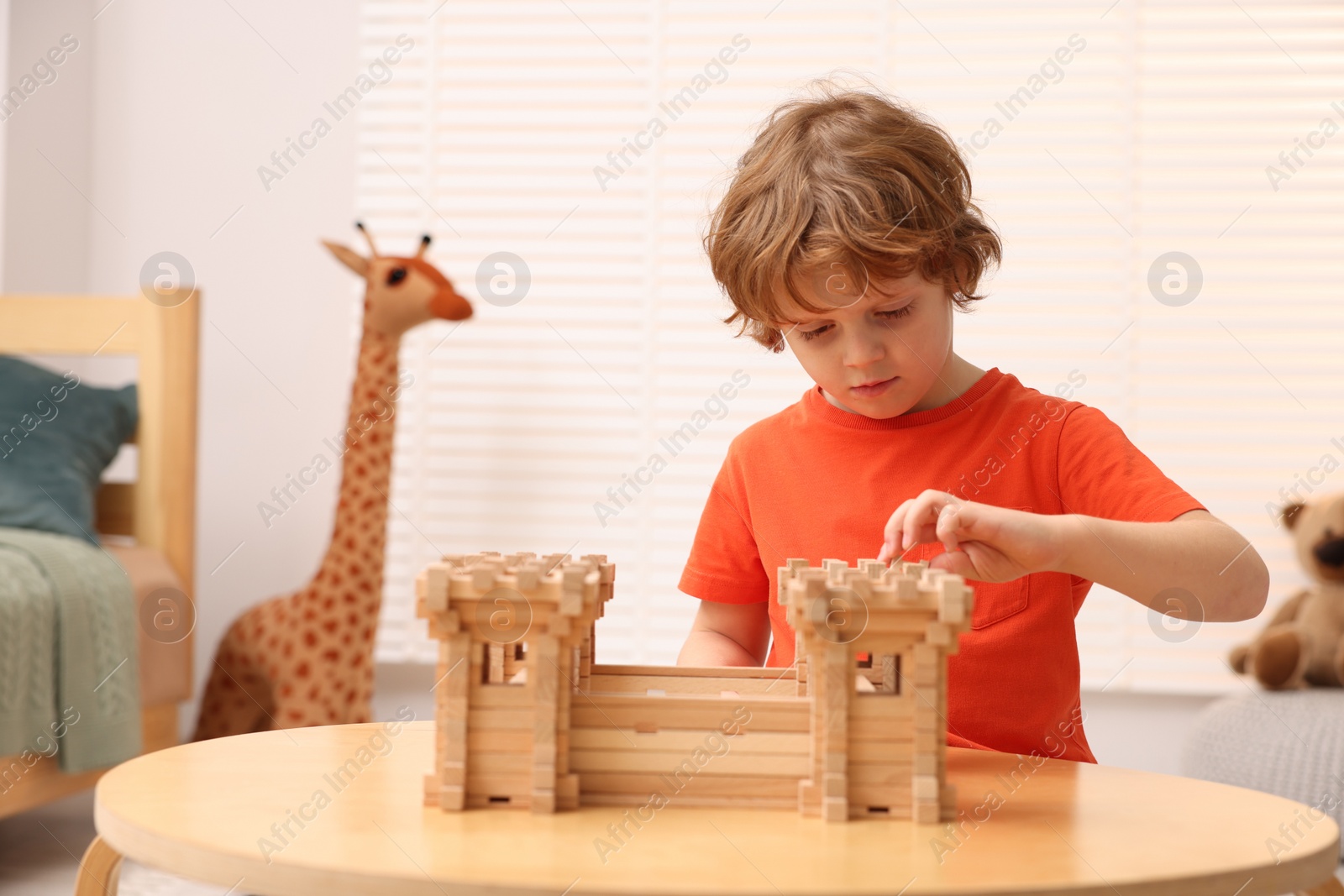 Photo of Cute little boy playing with wooden fortress at table in room. Child's toy