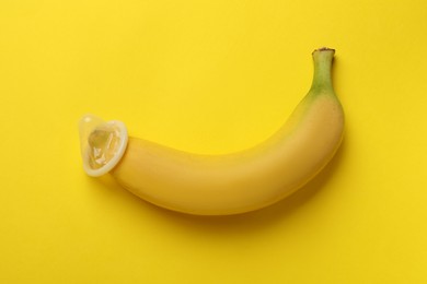 Photo of Banana with condom on yellow background, top view. Safe sex concept