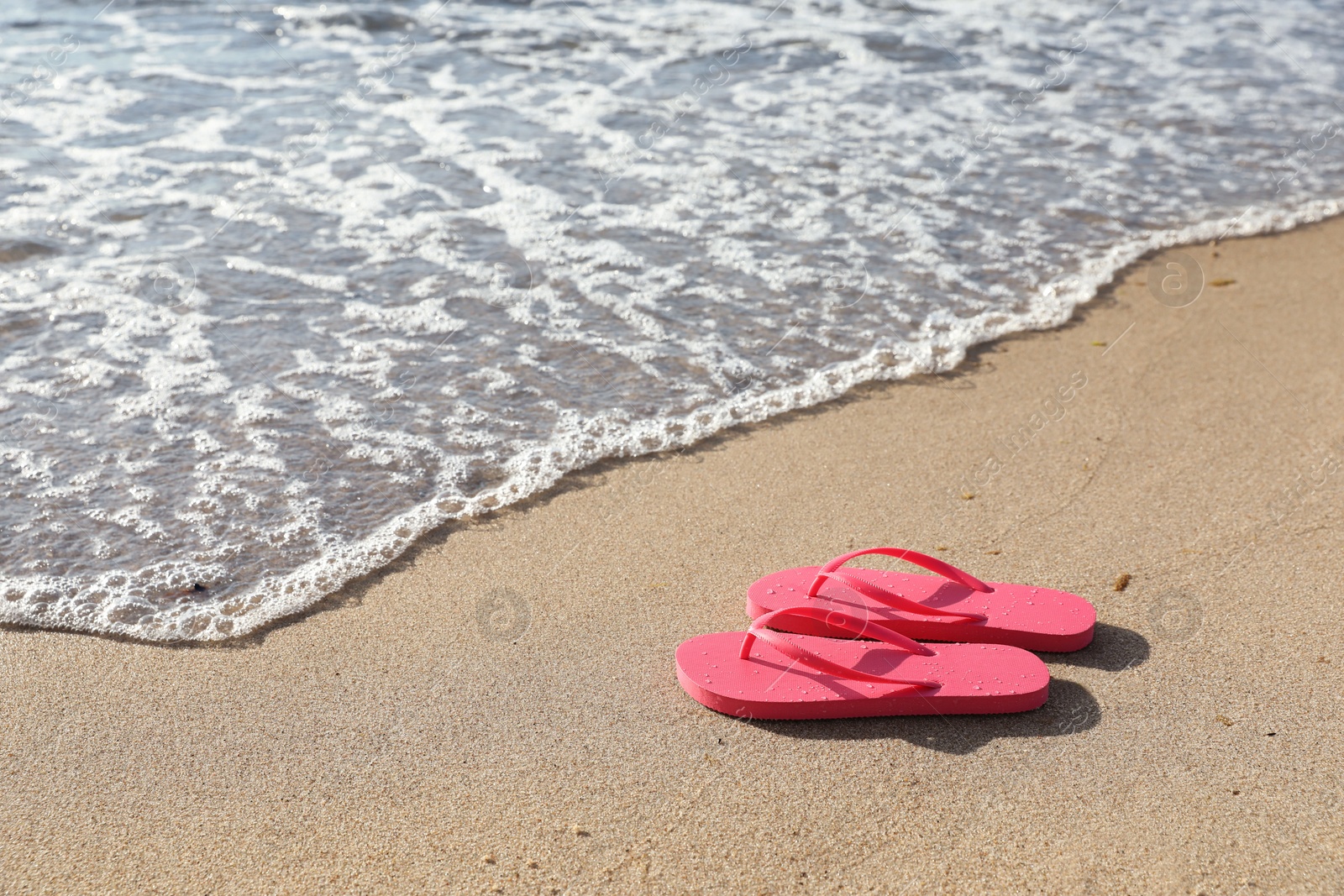 Photo of Stylish bright pink flip flops on sand near sea. Space for text