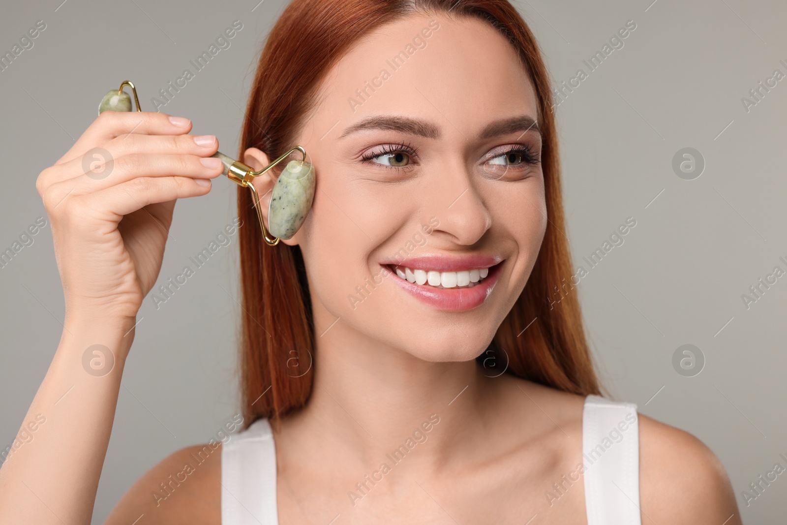 Photo of Young woman massaging her face with jade roller on grey background