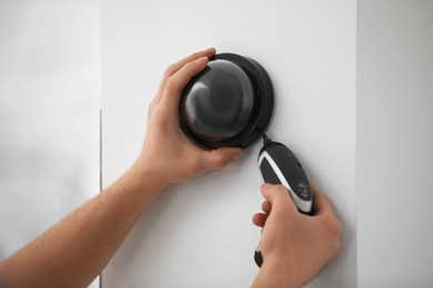 Technician installing CCTV camera on wall indoors, closeup