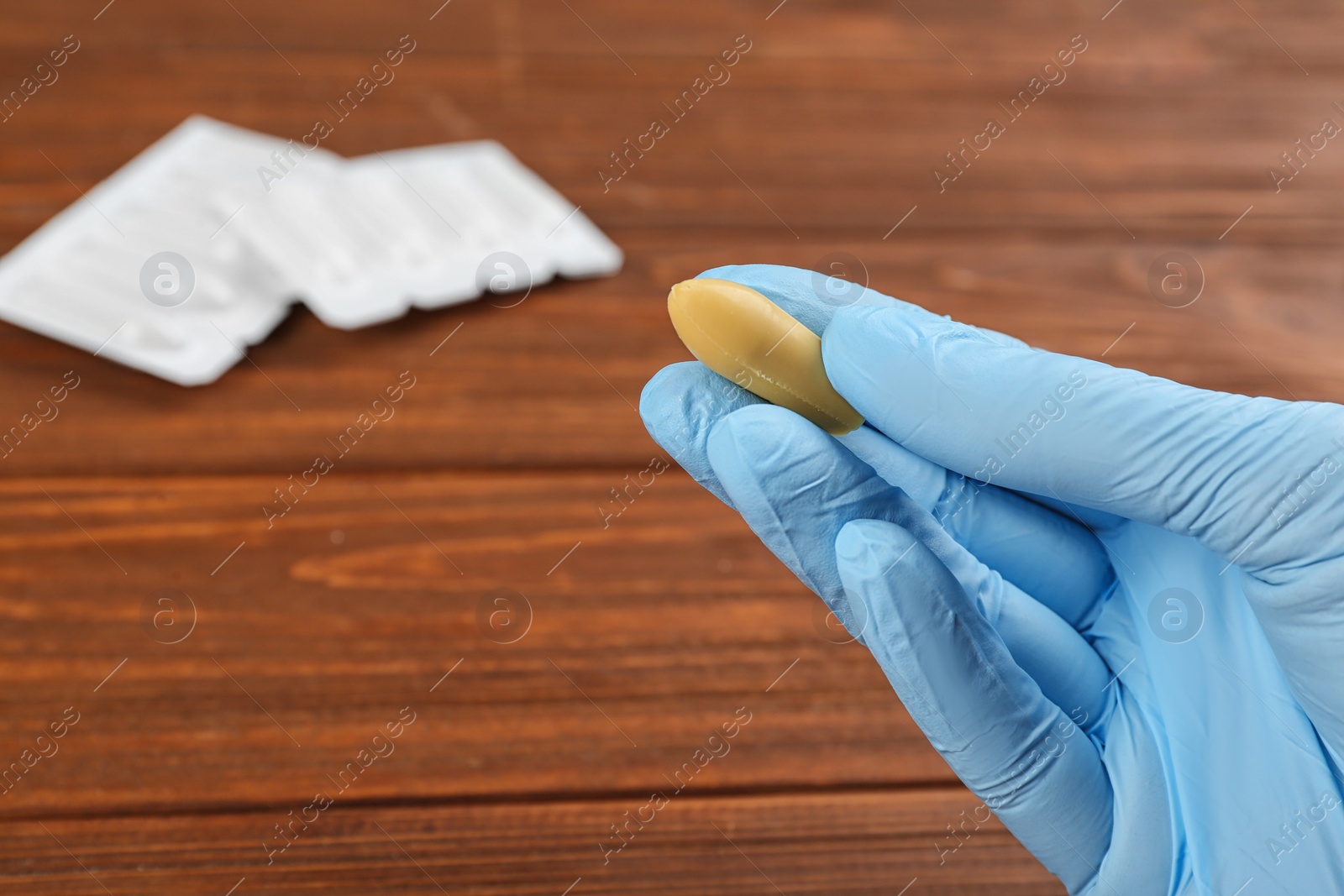 Photo of Woman holding suppository at wooden table, closeup. Hemorrhoid treatment