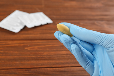 Woman holding suppository at wooden table, closeup. Hemorrhoid treatment
