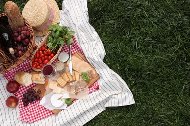 Photo of Picnic blanket with different products on green grass, top view. Space for text