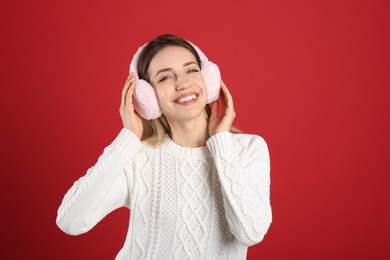 Happy woman wearing warm earmuffs on red background