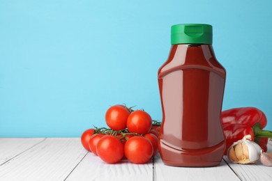 Photo of Bottle of tasty ketchup and ingredients on white wooden table. Space for text