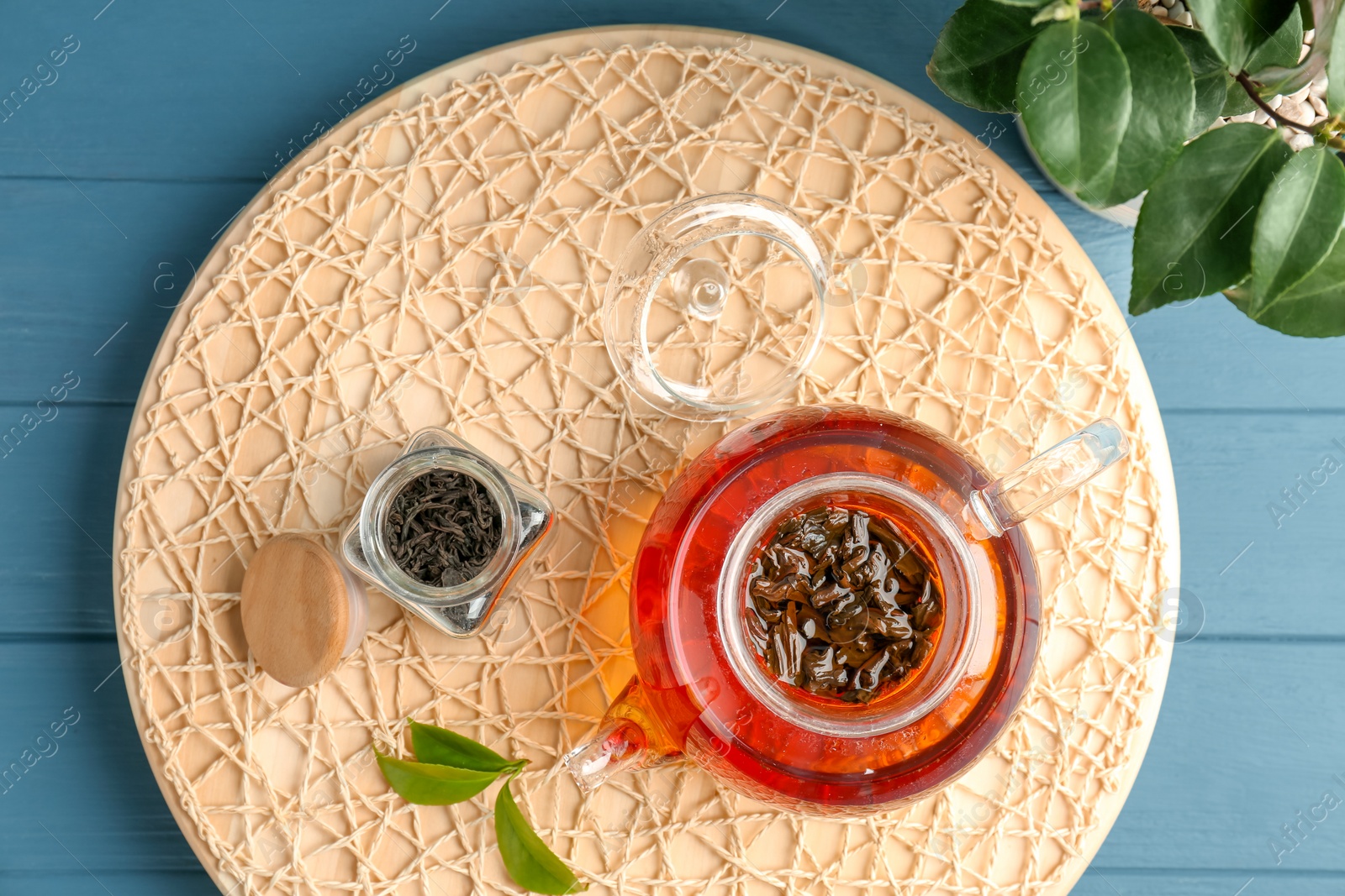 Photo of Teapot with hot aromatic tea, dry and fresh leaves on wicker mat, top view