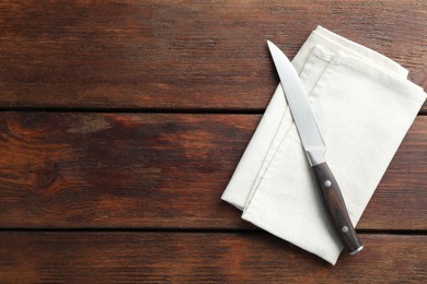 Photo of One sharp knife and napkin on wooden table, top view. Space for text