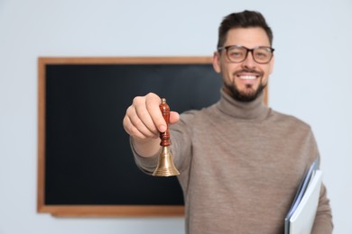 Photo of Teacher with school bell near black chalkboard indoors, space for text. Focus on hand