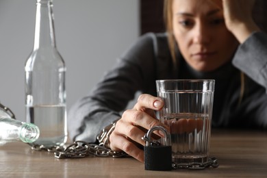 Alcohol addiction. Woman chained with glass of vodka at wooden table in room, focus on hand