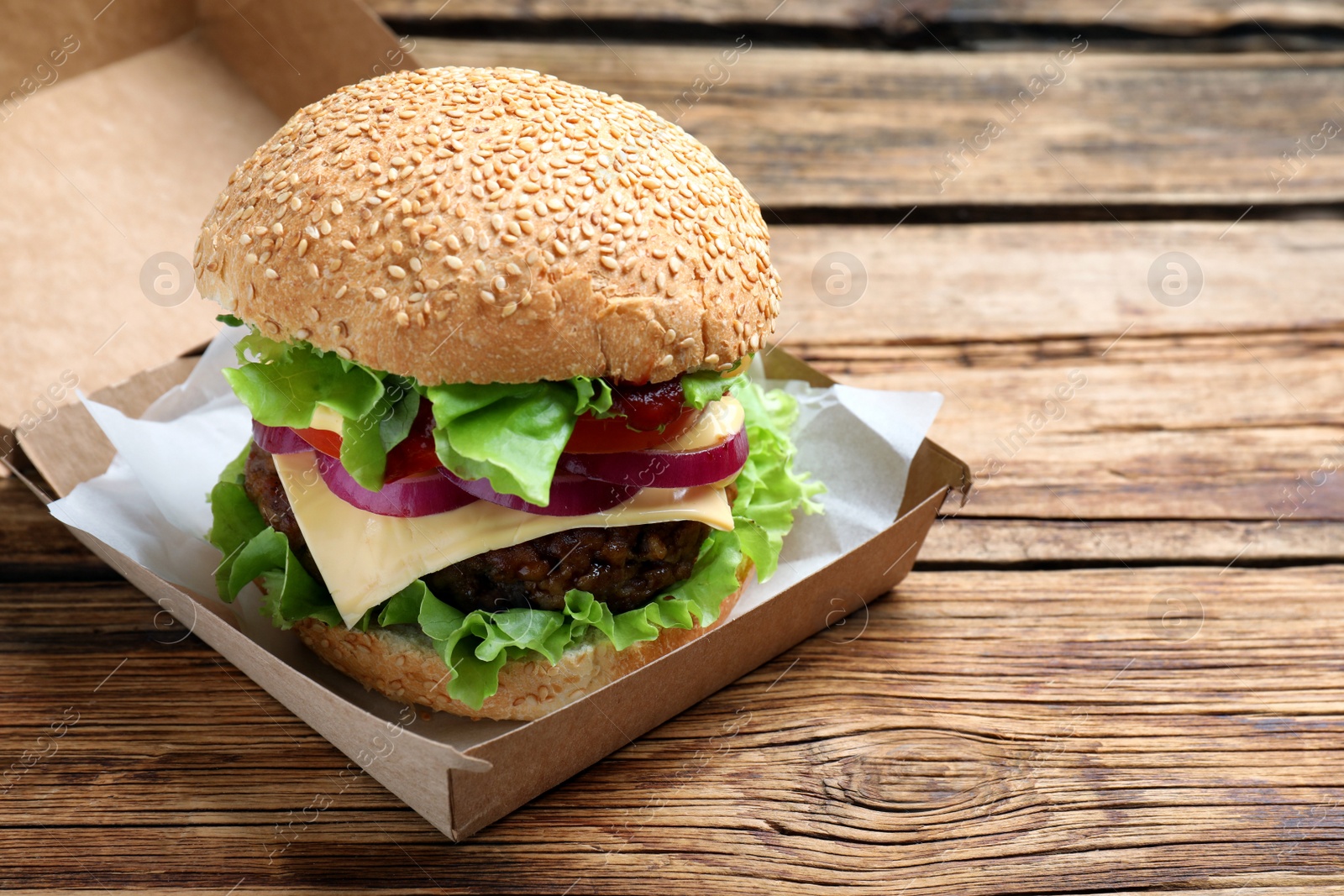 Photo of Delicious burger in cardboard box on wooden table