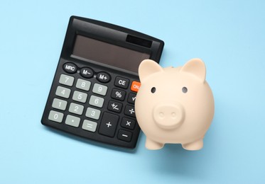 Calculator and piggy bank on light blue background, top view