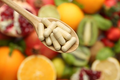 Photo of Vitamin pills in spoon over fresh fruits, top view