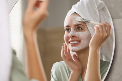 Photo of Woman applying face mask in frontmirror indoors. Spa treatments
