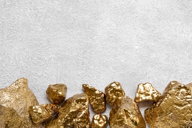 Photo of Pile of shiny gold nuggets on white textured table, flat lay. Space for text