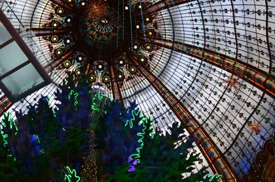 Paris, France - December 10, 2022: Beautiful stained glass dome and Christmas tree in Galeries Lafayette Haussmann, low angle view