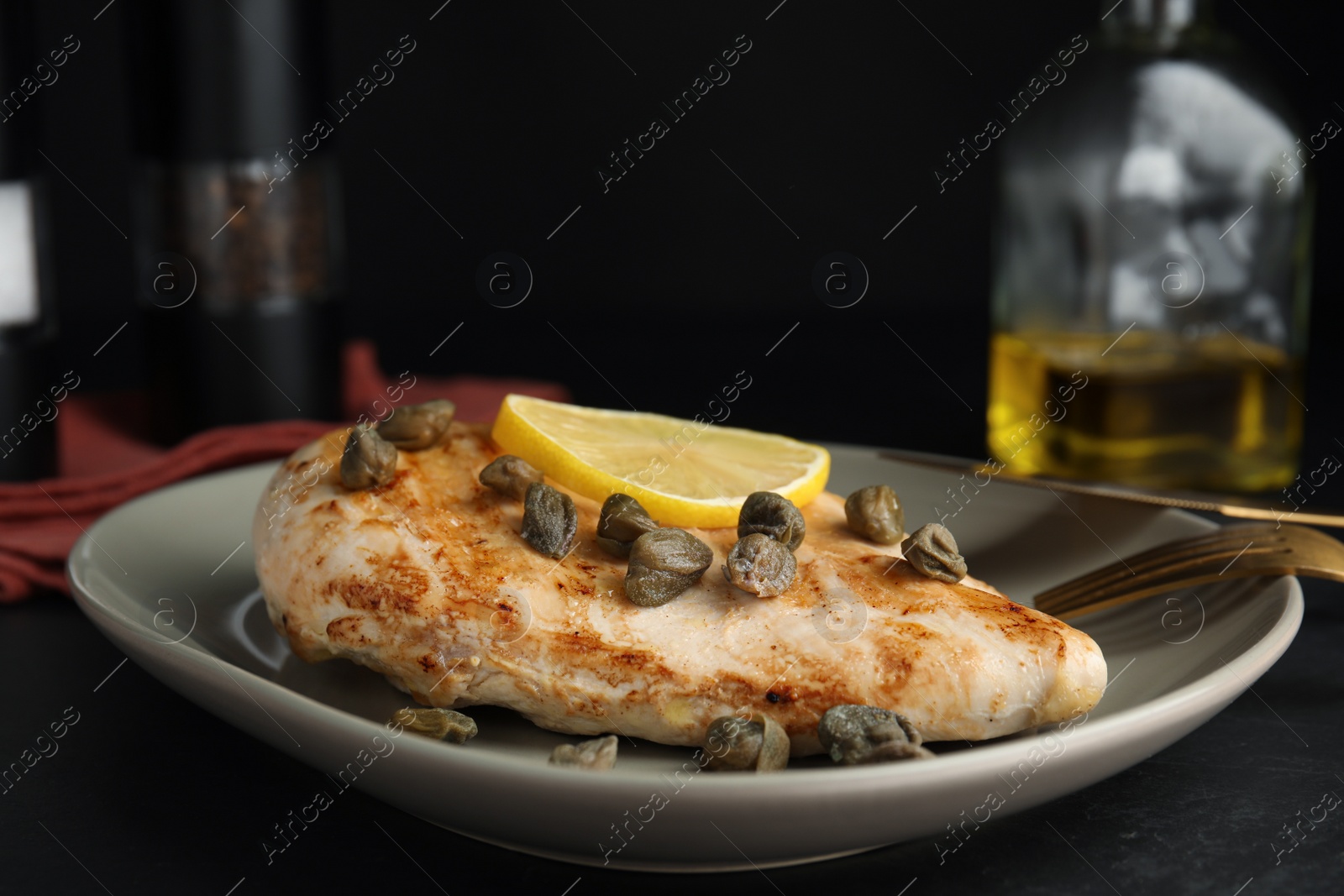 Photo of Delicious chicken fillet with capers and lemon served on black table, closeup