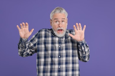 Portrait of surprised senior man on violet background