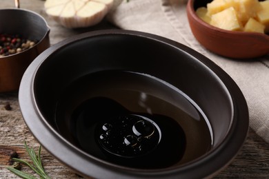 Bowl of balsamic vinegar with oil on old wooden table, closeup