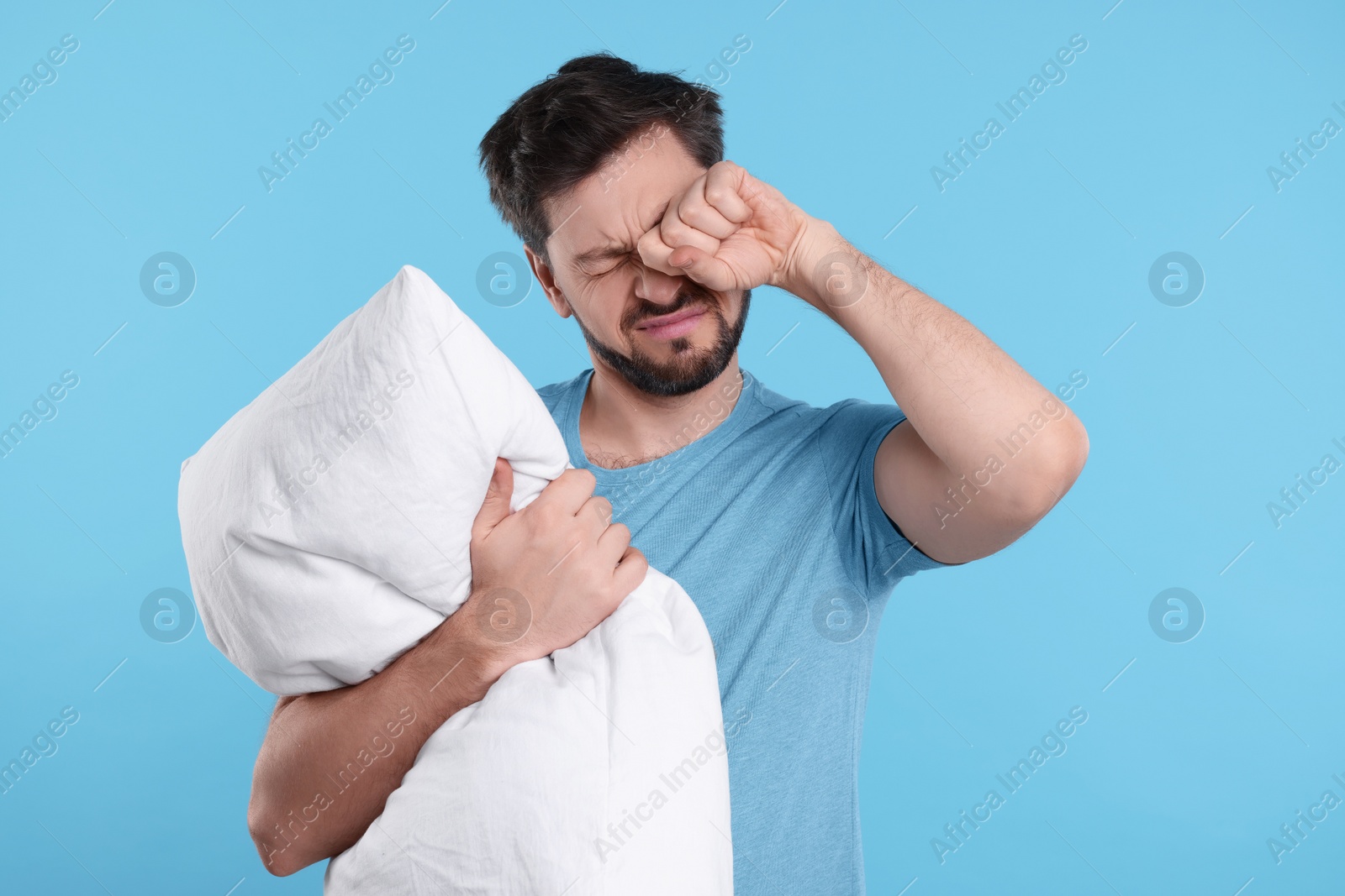 Photo of Tired man with pillow on light blue background. Insomnia problem